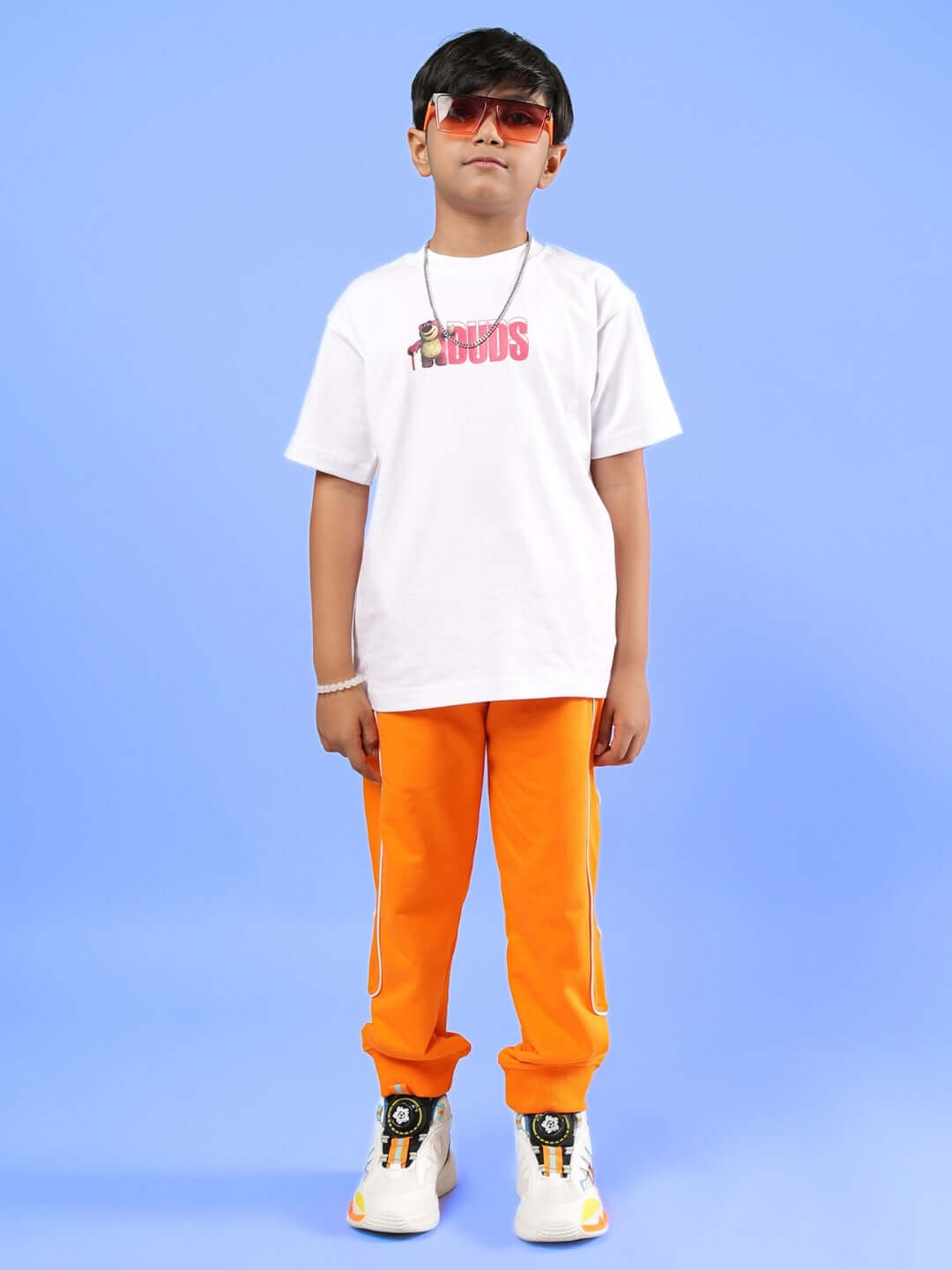 Child wearing white and orange LOTSO co-ord set, featuring a branded white t-shirt and vibrant orange pants, standing against a blue background.