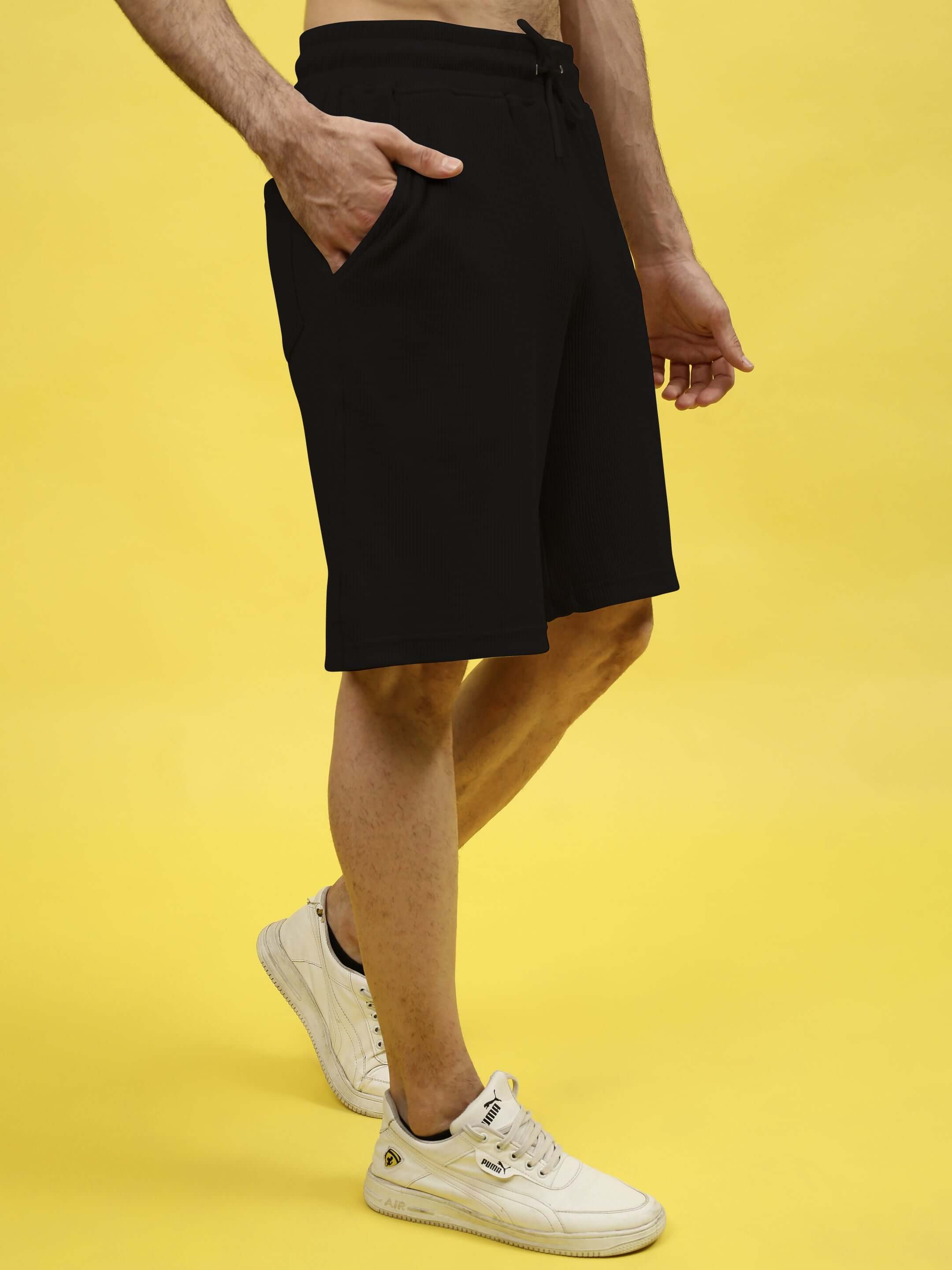 Man wearing black LOW-KEY solid co-ord shorts made from premium waffle 100% cotton fabric, standing against a yellow background.