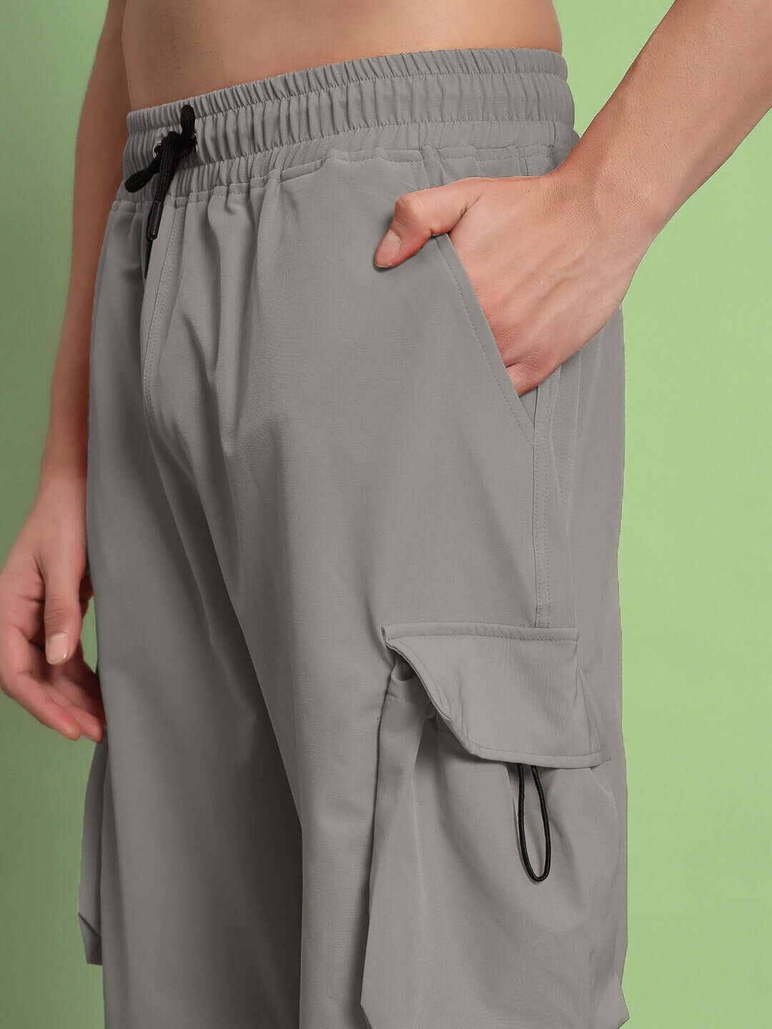 Close-up of MABEL relaxed fit grey cargo pants with pocket details against a green background.
