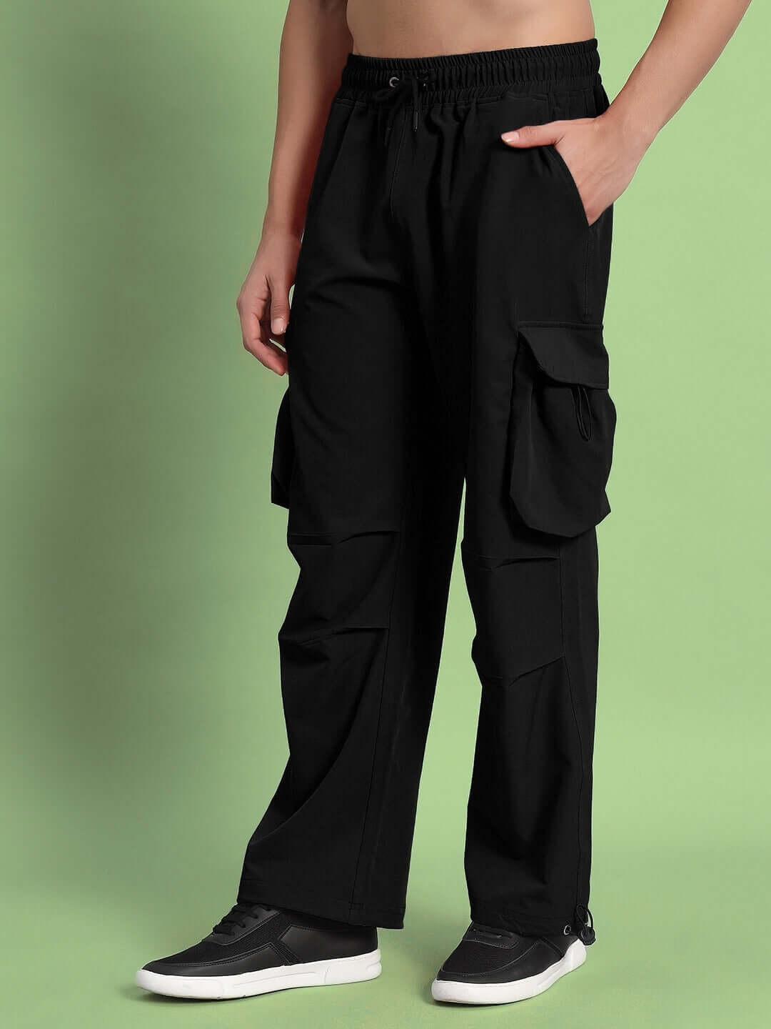 Person wearing black MABEL relaxed fit cargo pants with pockets, standing against a green background, showcasing comfortable casual wear.