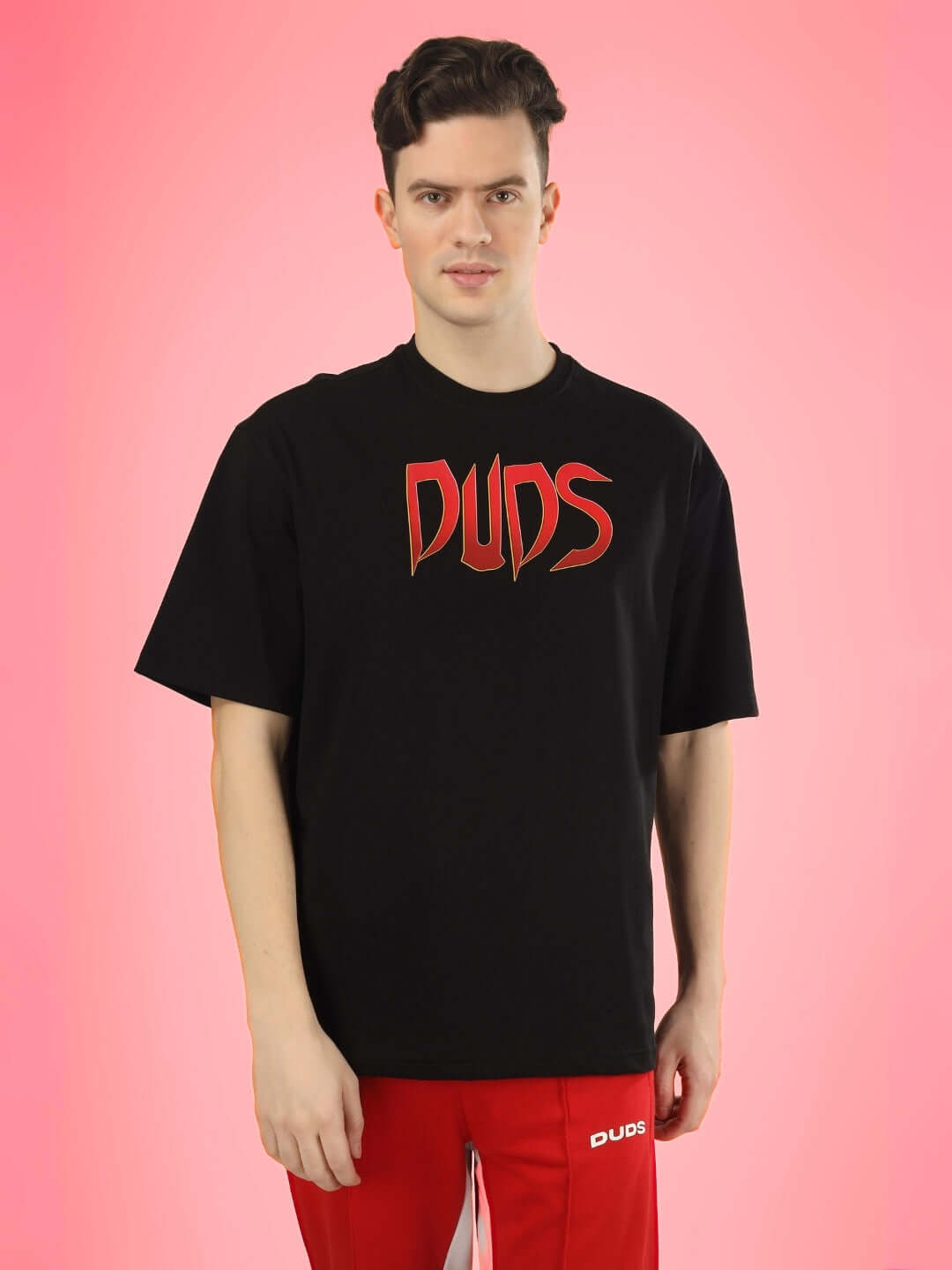 Man wearing a black oversized 'MAFIA' T-shirt with red 'DUDS' logo, against a pink background.