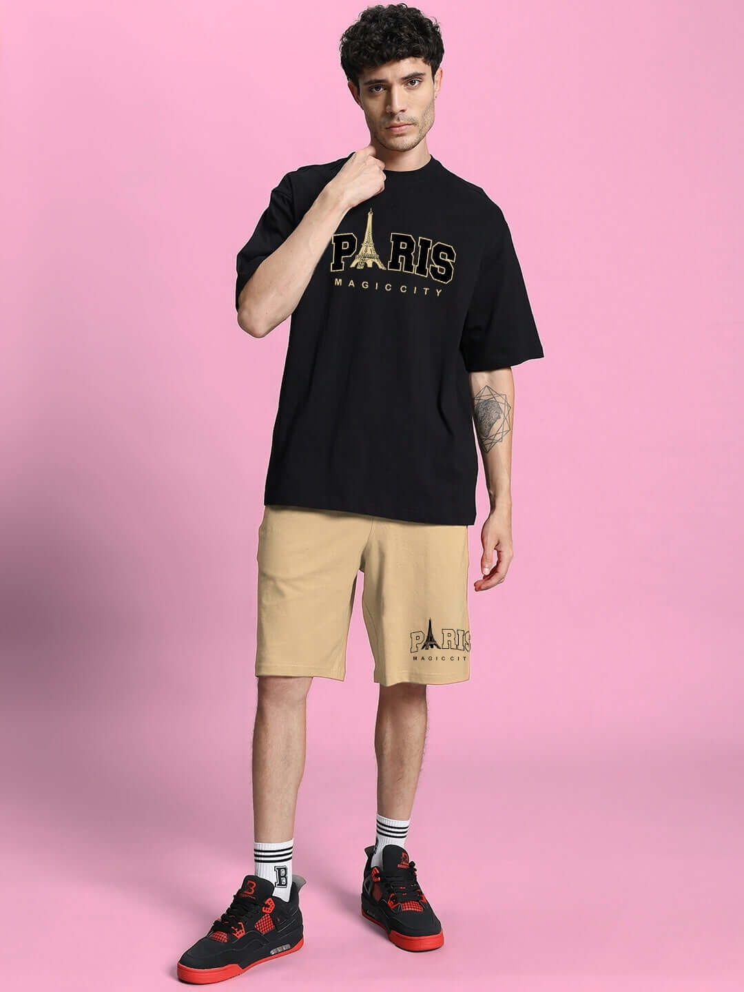 Model wearing MAGIC CITY SUMMER CO-ORD SET in black and beige, featuring a t-shirt and shorts, against a pink backdrop.