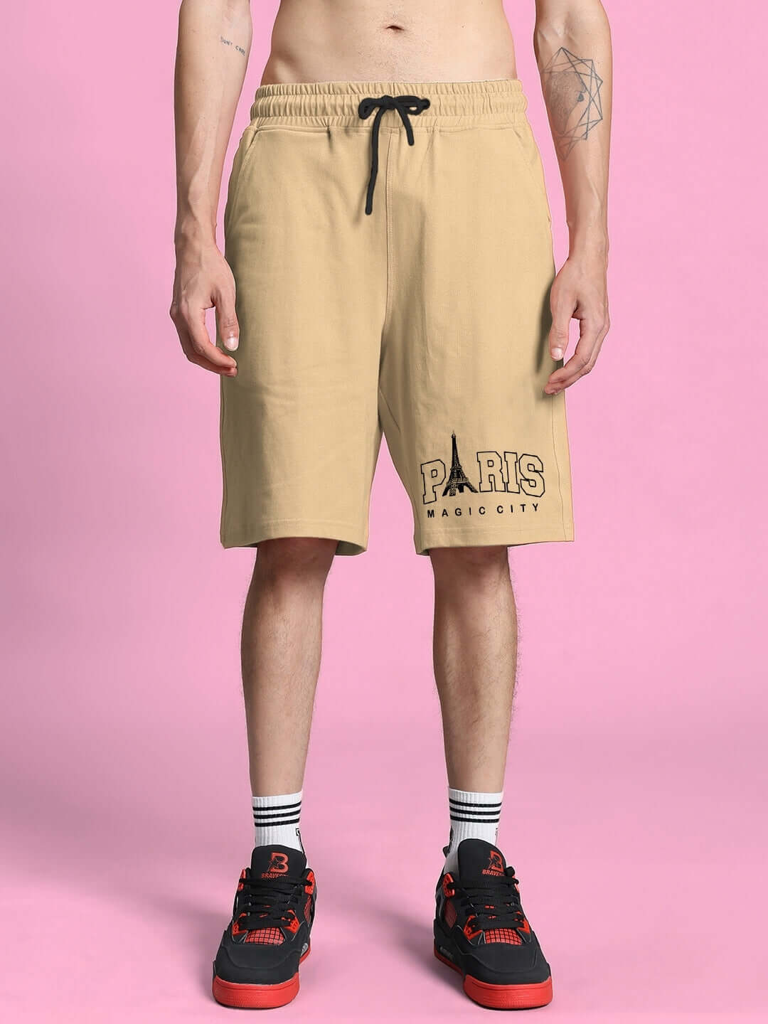 Beige shorts featuring Paris Magic City logo, worn with black and red sneakers against a pink background.