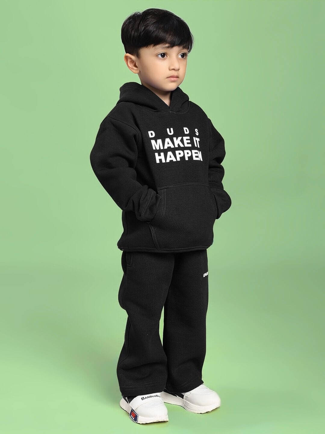 Child wearing MAKE IT HAPPEN FLEECE CO-ORD FOR BOYS AND GIRLS BLACK on a green background.