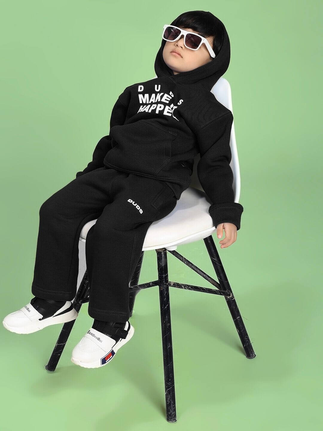 Child wearing MAKE IT HAPPEN FLEECE JOGGER FOR BOYS AND GIRLS BLACK sitting on a chair with sunglasses