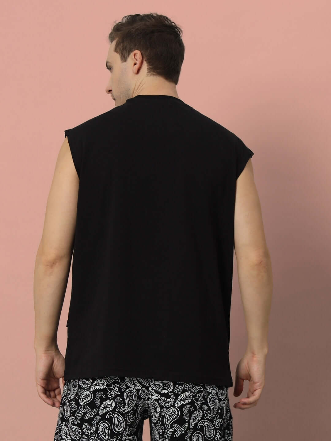 Back view of a person wearing a Mandla black gym t-shirt, showcasing sleeveless design against a pink background.