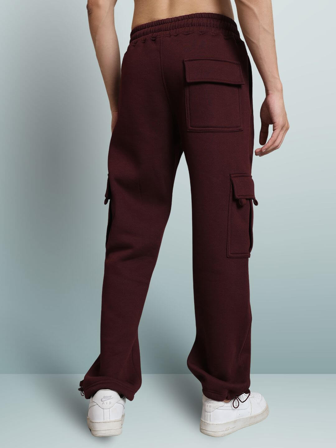 Back view of maroon relaxed fit cargo fleece pants with multiple pockets, worn by a model with white sneakers.