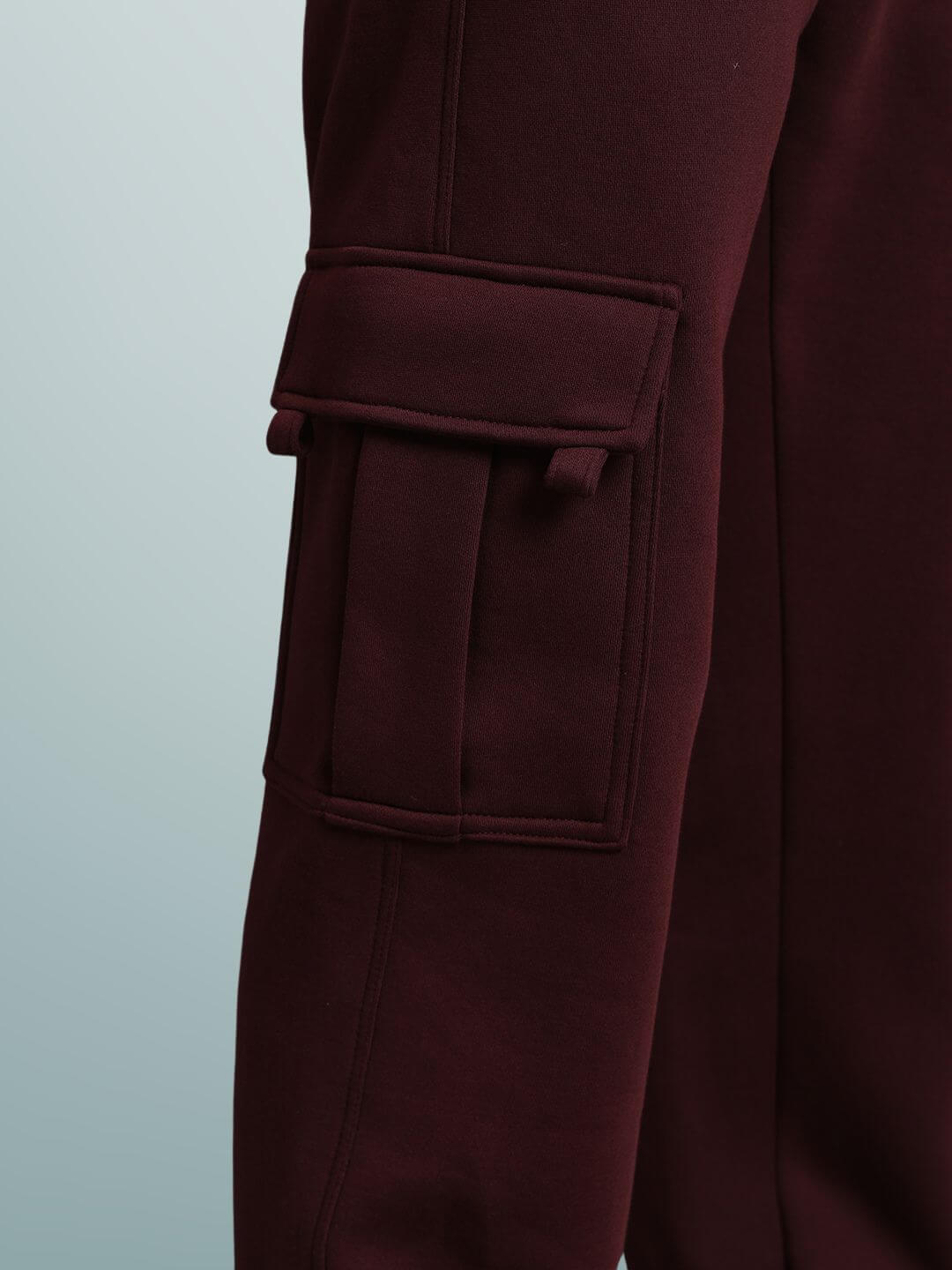 Close-up of maroon relaxed fit cargo fleece pant with detailed pocket design on fabric.
