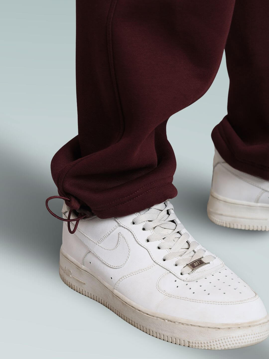 Close-up of maroon relaxed fit cargo fleece pants paired with white sneakers on a light background