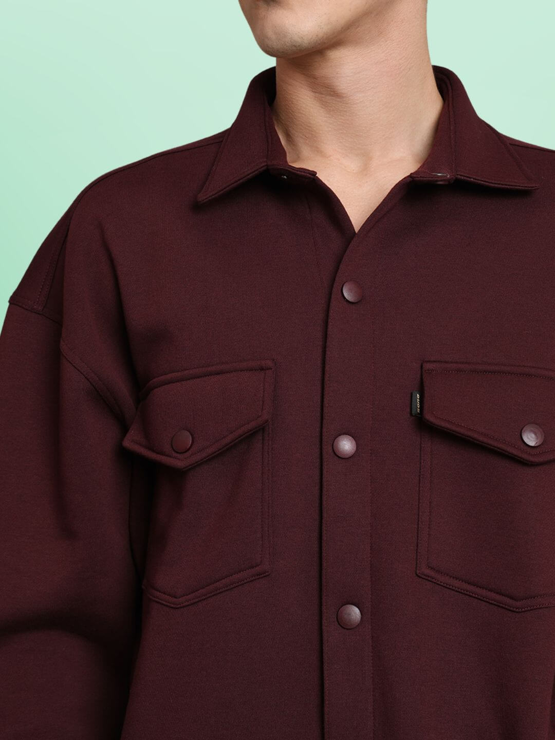 Maroon relaxed fit fleece overshirt with full sleeves and button-down front, featuring dual chest pockets on a green background.