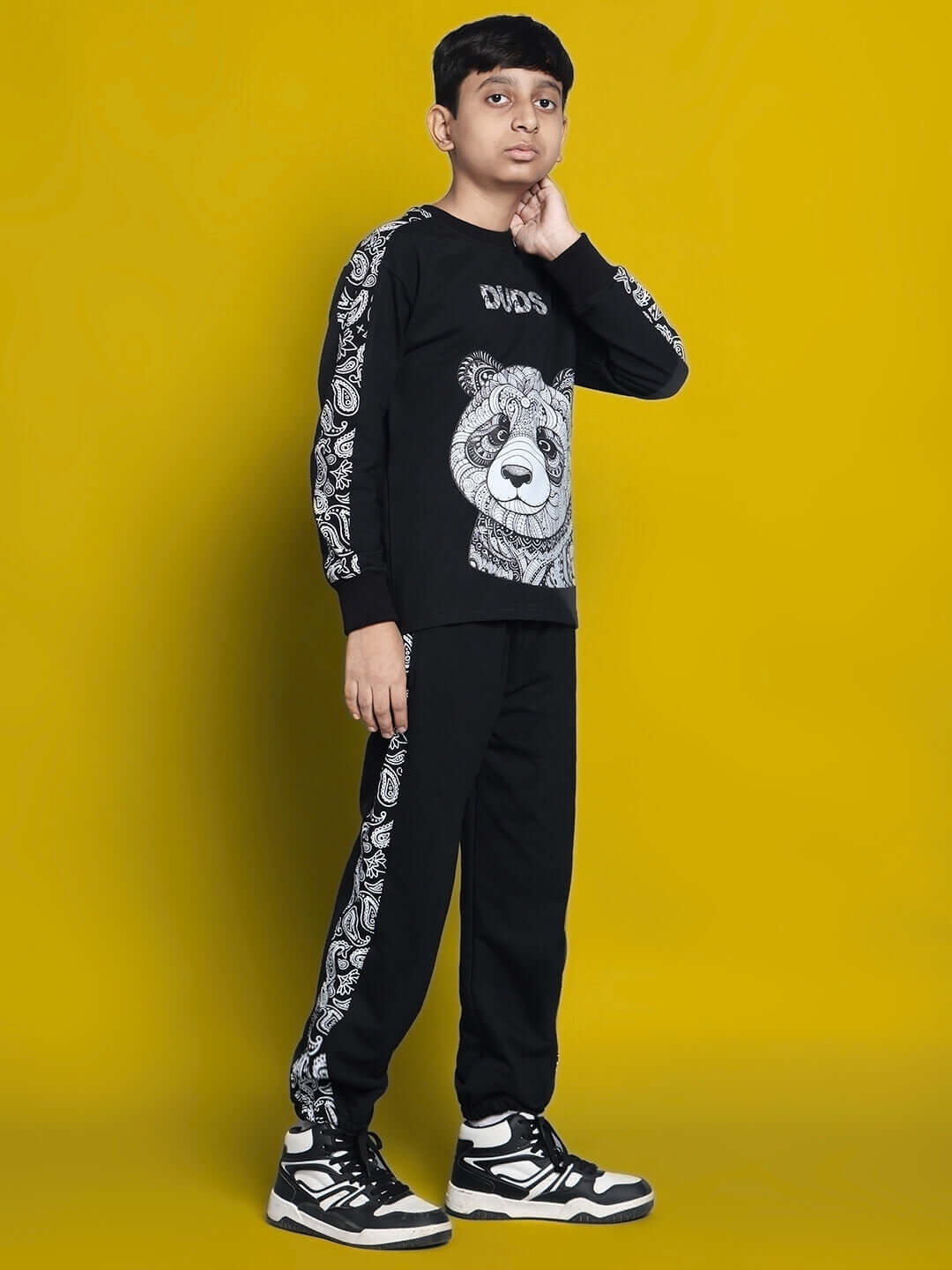 Child wearing MASHA co-ord set for boys and girls in black, featuring a panda design, standing against a yellow background.
