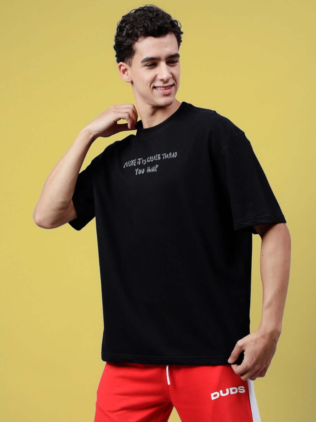 Model wearing MAYBE IT IS EASIER THAN YOU THINK black oversized t-shirt, made of premium cotton French terry, with red pants.