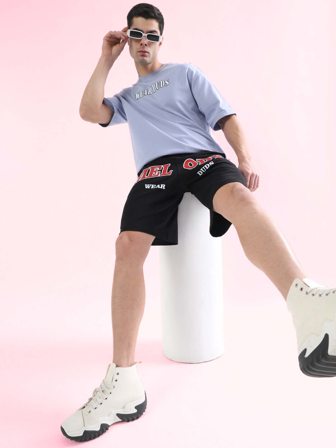 Model wearing Melody Regular Fit Black Shorts with graphic design, showcasing casual streetwear style against a pink background.