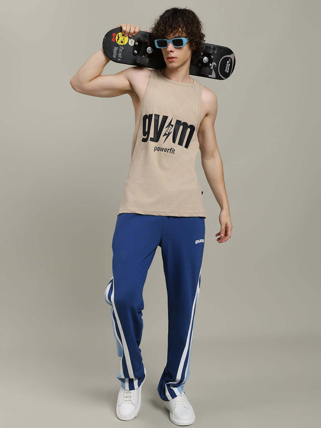 Model wearing blue RIO ONE Relaxed Fit Joggers and beige tank top, holding a skateboard, stylish casual look.