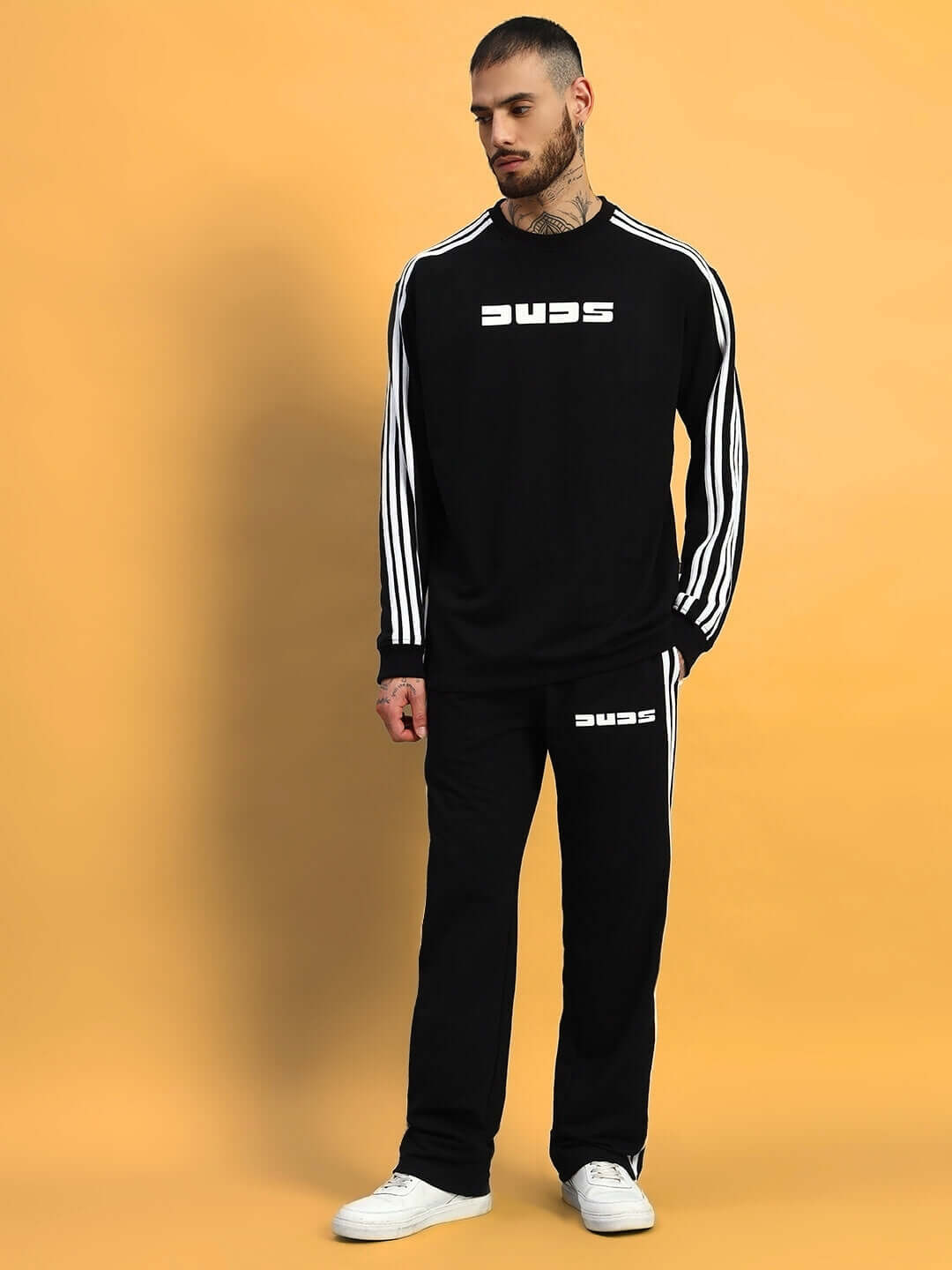 Model wearing black oversized parka co-ord set with white stripes, featuring unisex joggers with elastic waistband on a yellow background.