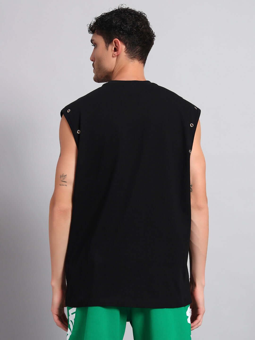 Back view of man wearing ALVEN Oversized Black T-Shirt, showcasing sleeveless design with green shorts.