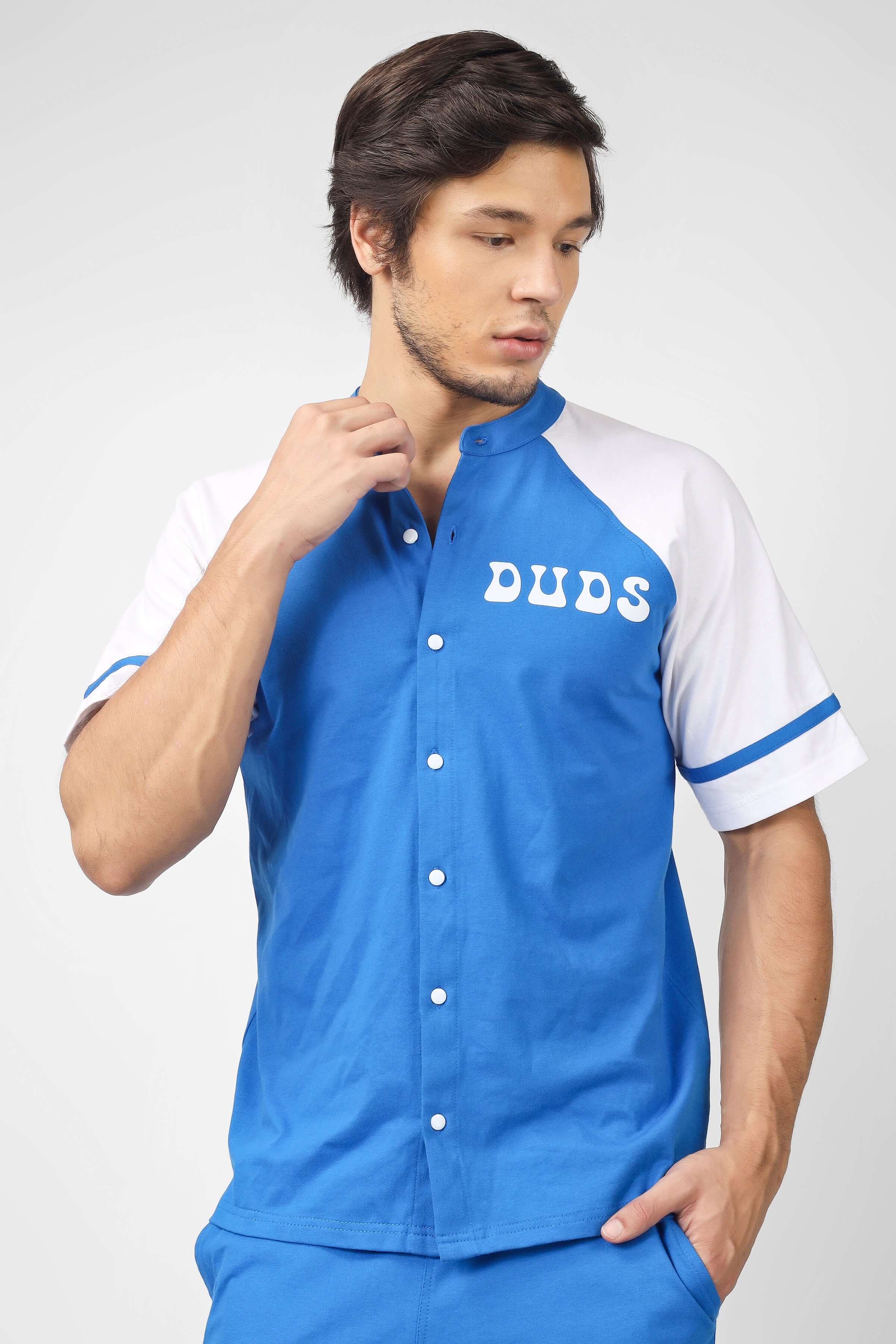 Man wearing blue and white short-sleeve shirt with 'DUDS' text on the front, styled with matching blue pants, standing against a plain background.
