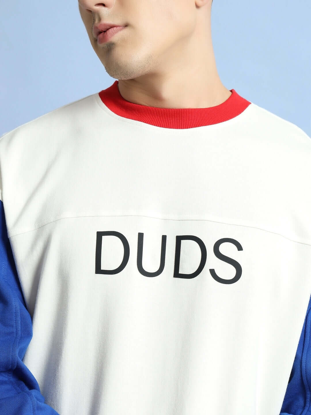 Man wearing DUDS Candy Crush oversized sweatshirt in white, red, and blue with bold lettering.