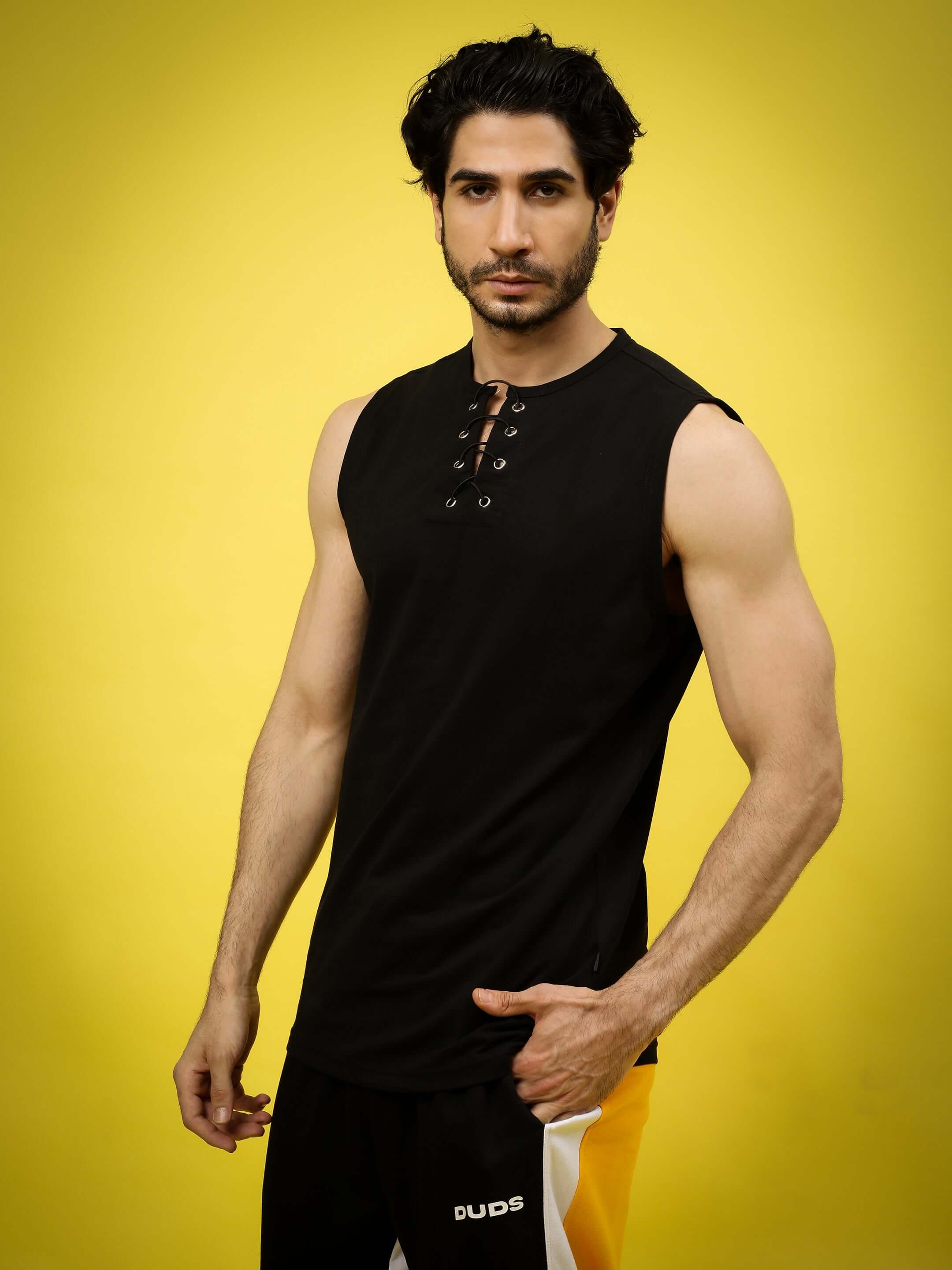 Man wearing black sleeveless Pinnacle regular fit t-shirt with lace-up front, against a yellow background.