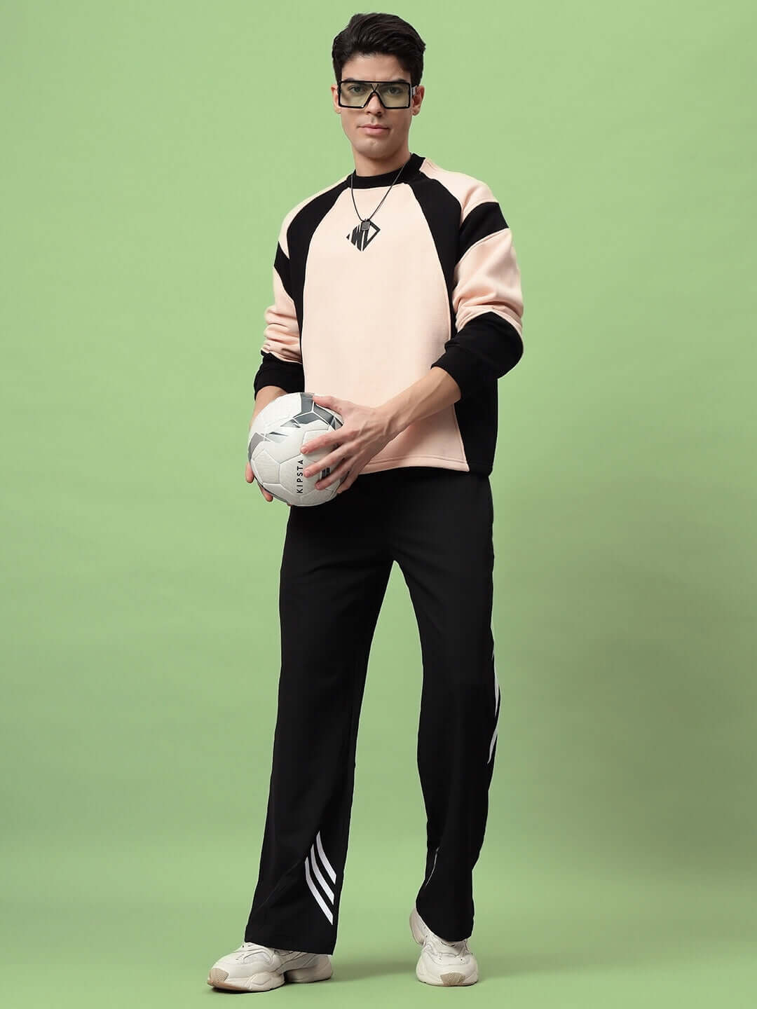 Model wearing black relaxed fit cargo pants, holding a soccer ball, standing against a green background.