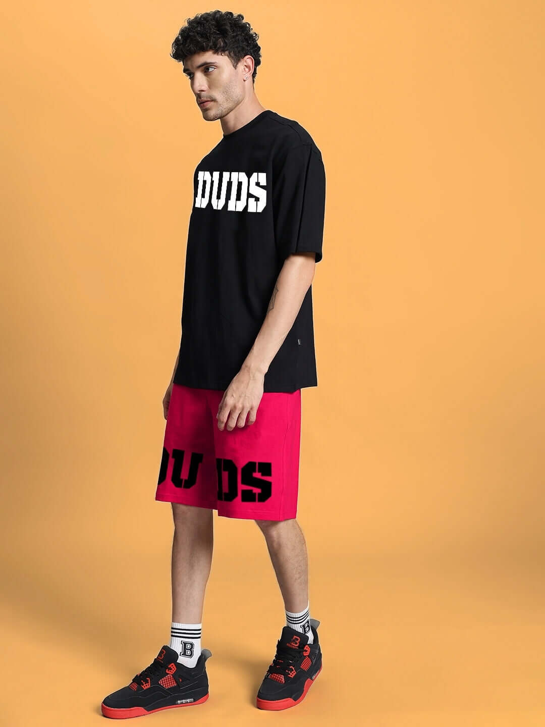 Model wearing black and pink CHERRY BLOSSOM SUMMER CO-ORD SET with 'DUDS' print, showcasing casual style on orange background.