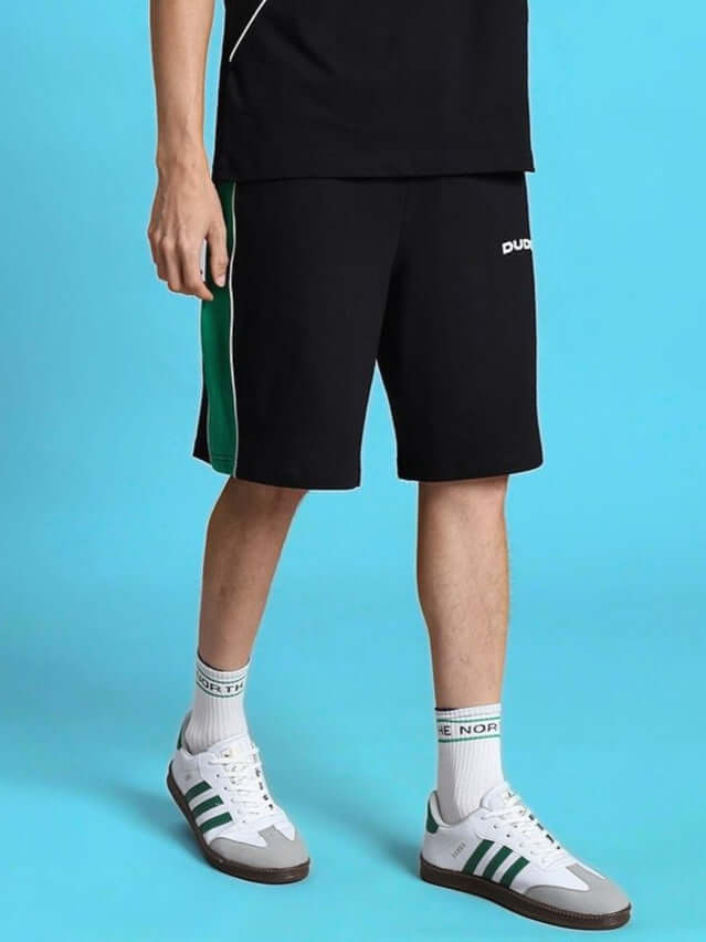 Model wearing METEORIC REGULAR FIT SHORTS BLACK and white sneakers against blue background