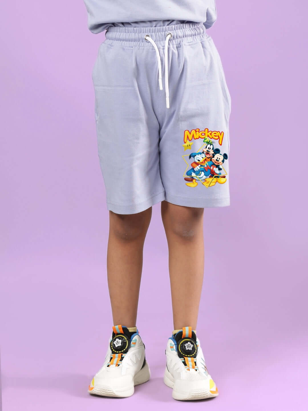 Child wearing MICKEY DINGO CO-ORD FOR BOYS & GIRLS LAVENDER with cartoon print shorts and colorful sneakers.