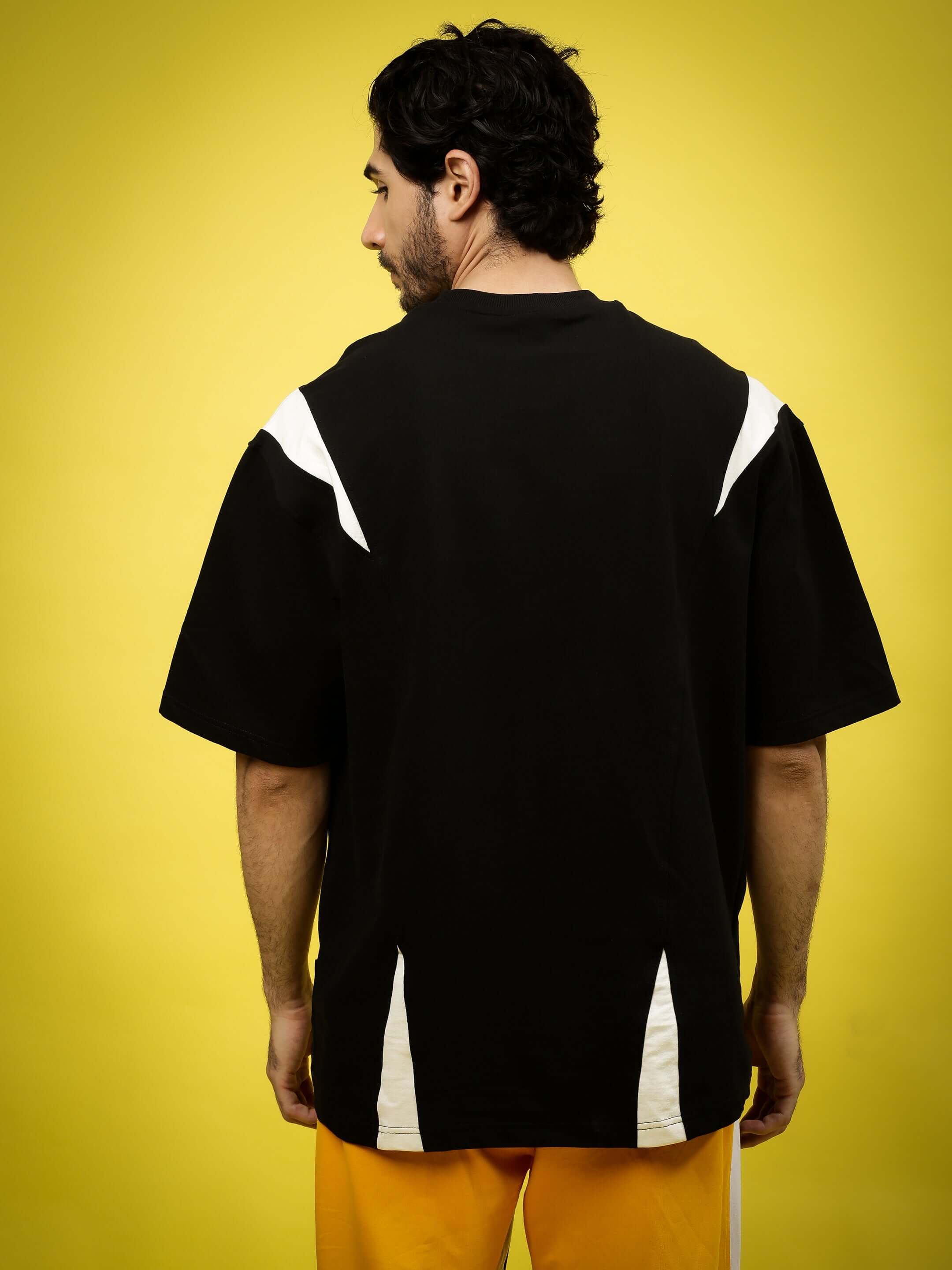 Back view of a black and white oversized T-shirt made from premium cotton fabric, worn by a male model against a yellow background.