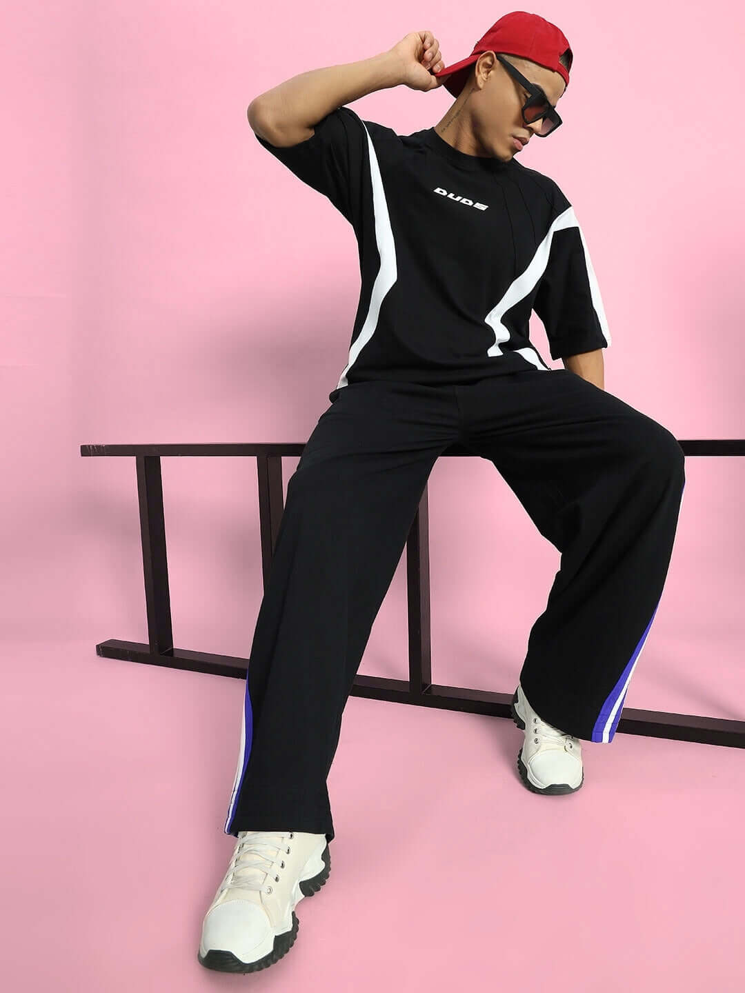 MILANO RELAXED-FIT JOGGERS BLACK-BLUE Model wearing Milano relaxed-fit joggers in black-blue, styled with a black shirt and white sneakers, against a pink backdrop.