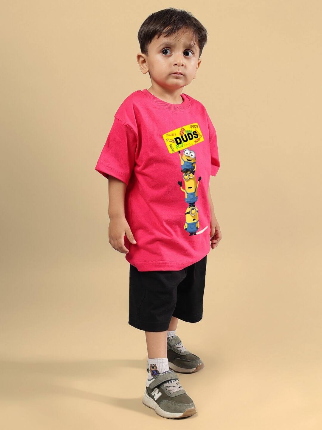 Child wearing Minion cartoon co-ord set in pink and black, featuring a Minion-printed T-shirt and black shorts, standing against a beige background.