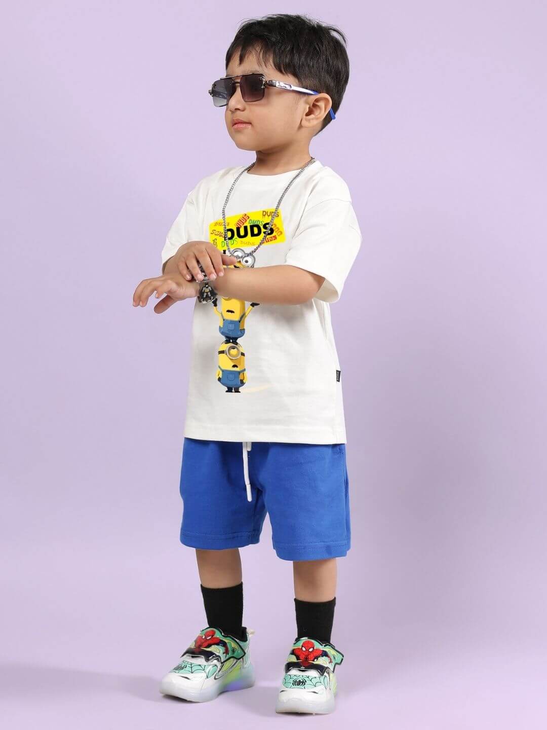Boy wearing Minion cartoon co-ord set with off-white T-shirt and blue shorts, standing stylishly in sunglasses.