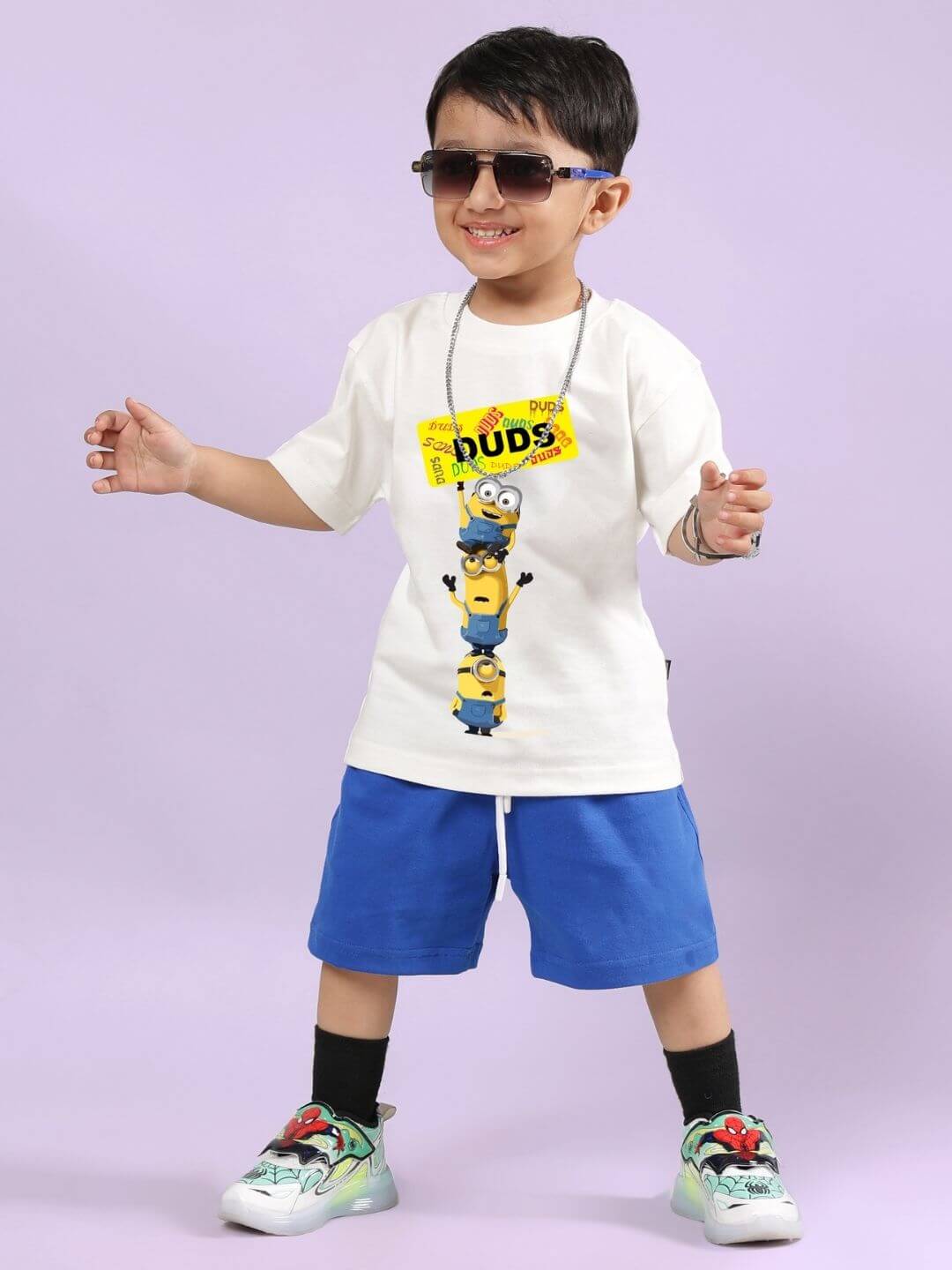 Boy wearing Minion cartoon off-white T-shirt and blue shorts set, smiling with sunglasses.