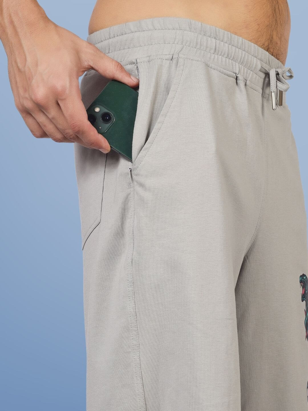 A person placing a smartphone in the pocket of grey regular fit shorts with a moaning tigress design, showcasing comfort and practicality.