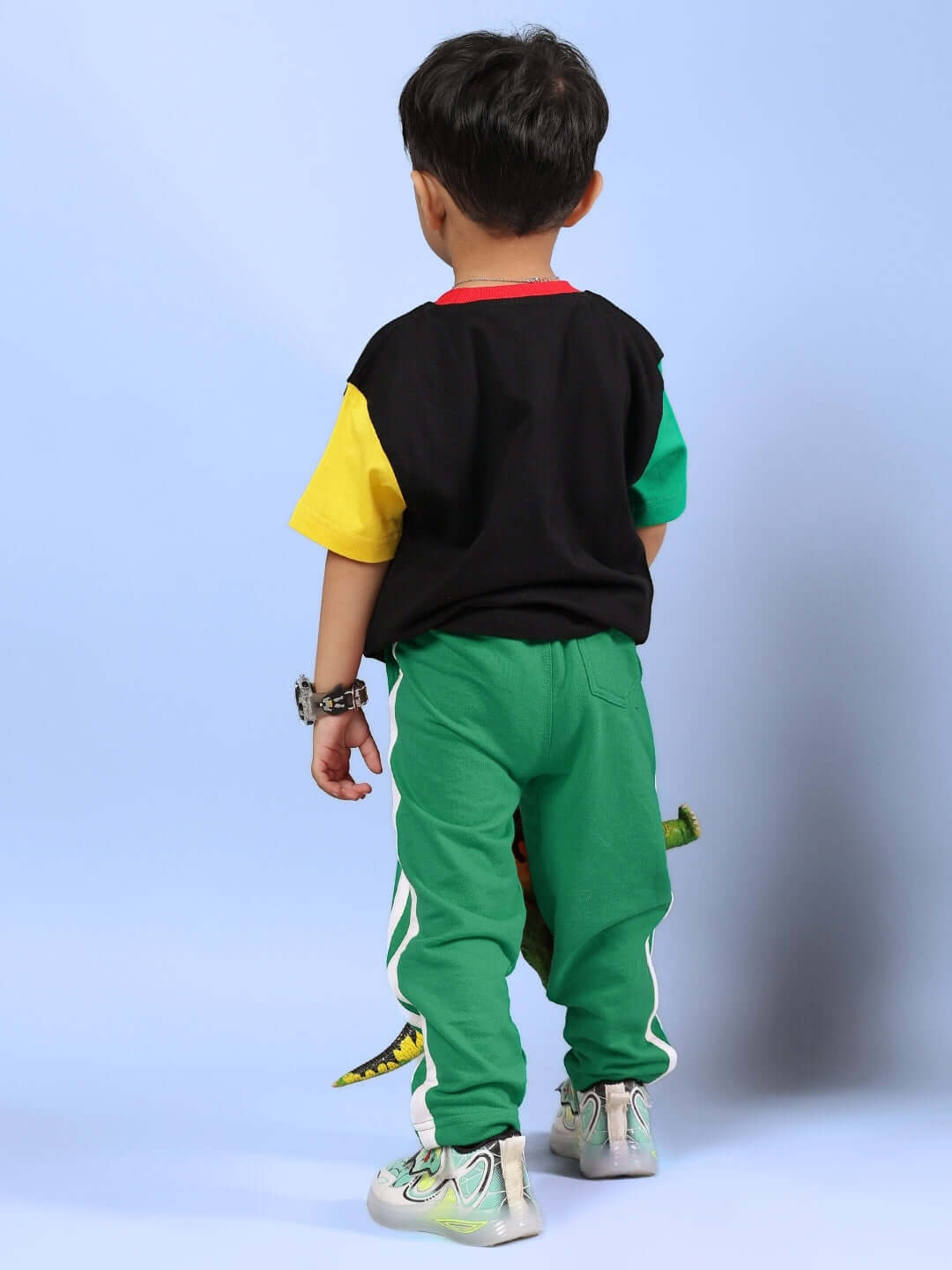 Child wearing MOCHA CO-ORD FOR BOYS & GIRLS BLACK GREEN, showing back view with colorful shirt and green pants on a blue background.