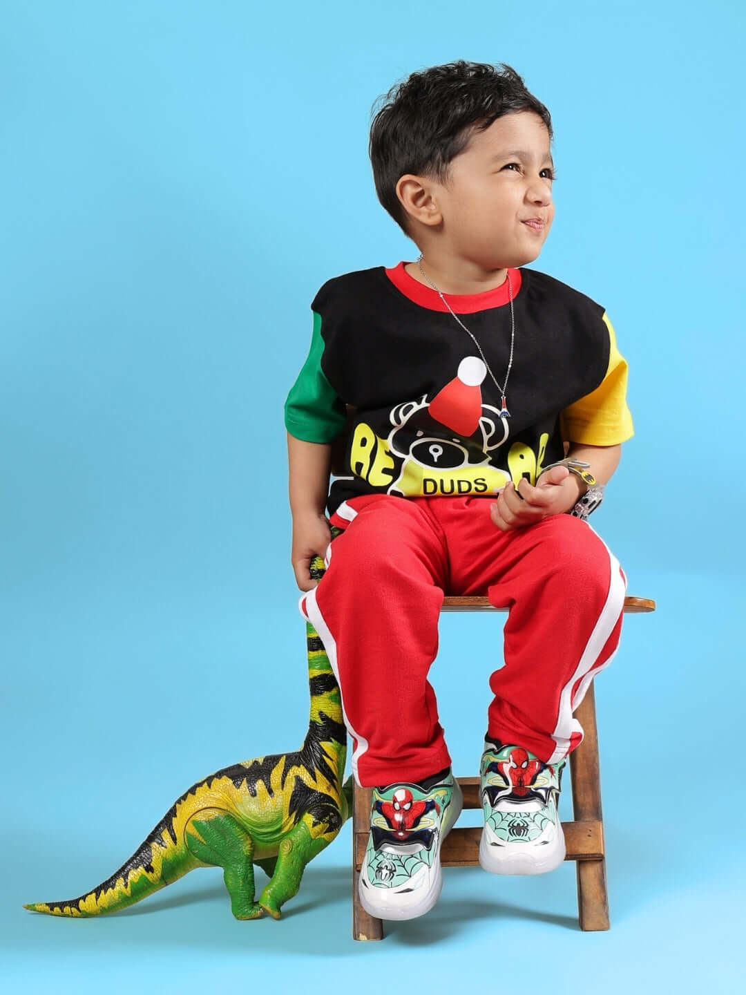 Toddler wearing MOCHA co-ord in black and red by DUDS, sitting on a stool with a toy dinosaur, showcasing vibrant fashion for kids.