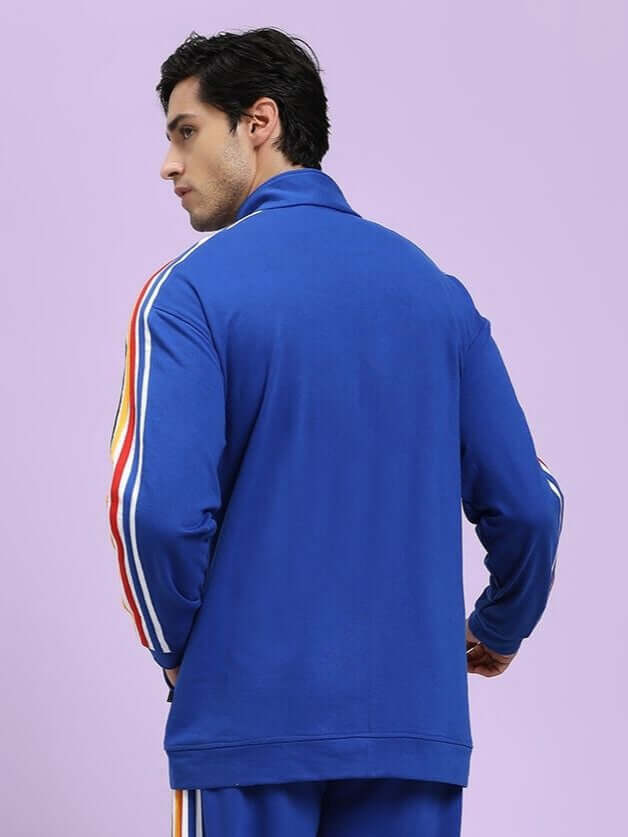 MODERN EDGE MULTI-STRIPE JACKET ROYAL BLUE Person wearing a blue tracksuit with colorful stripes on a light purple background