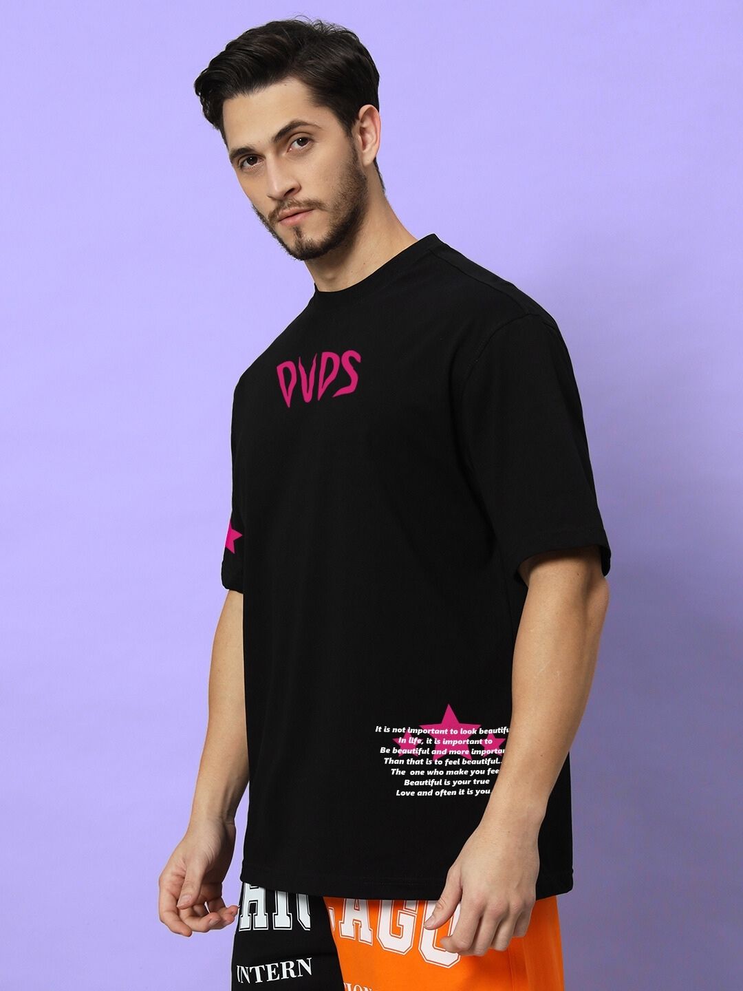 Man wearing MODERN LOVE OVER-SIZED T-SHIRT BLACK with vibrant print, posing against a purple background