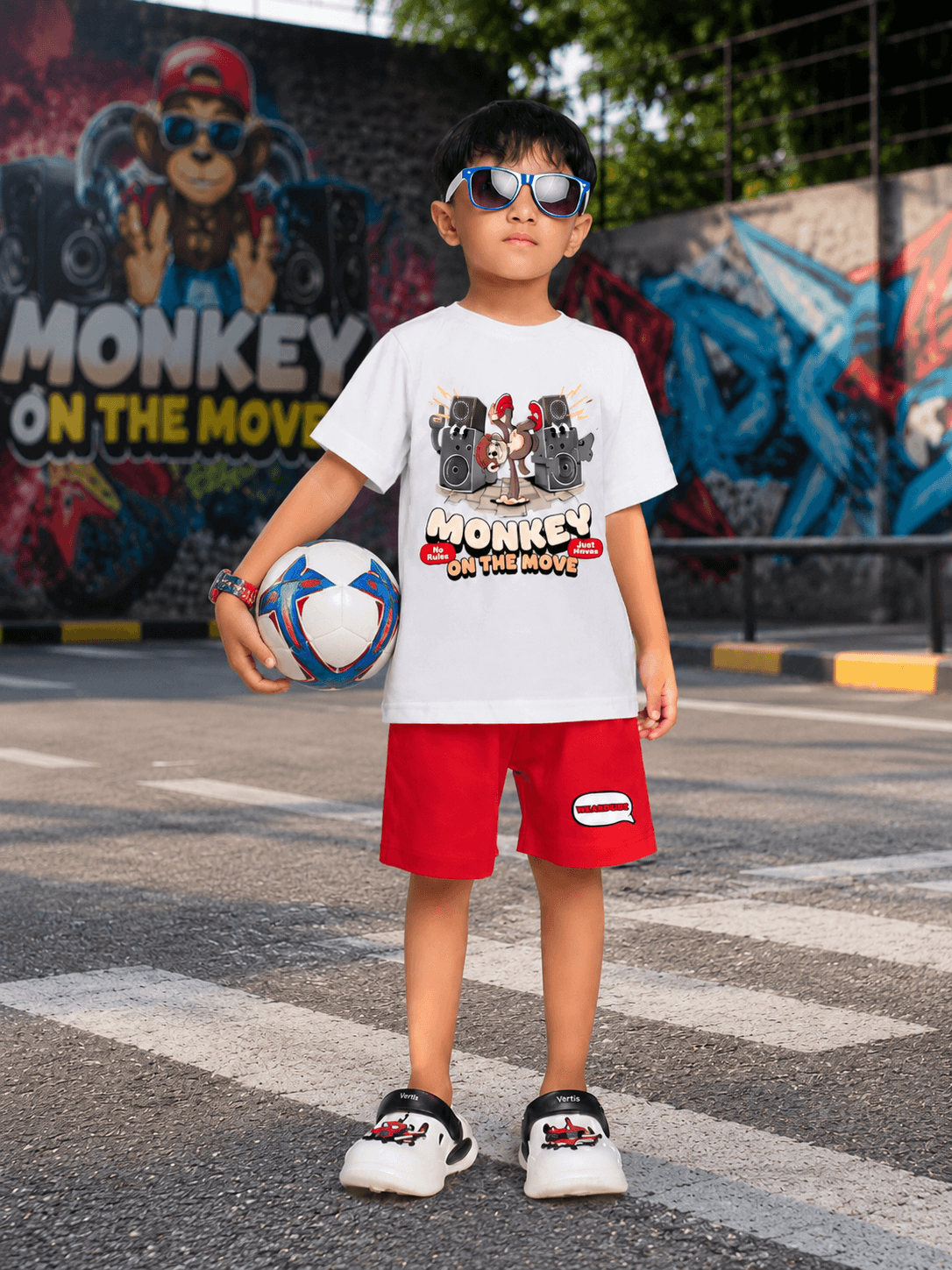 MONKEY BEATS COOL SHORTS FOR BOYS GIRLS RED worn by a child holding a soccer ball in a playful outdoor setting.