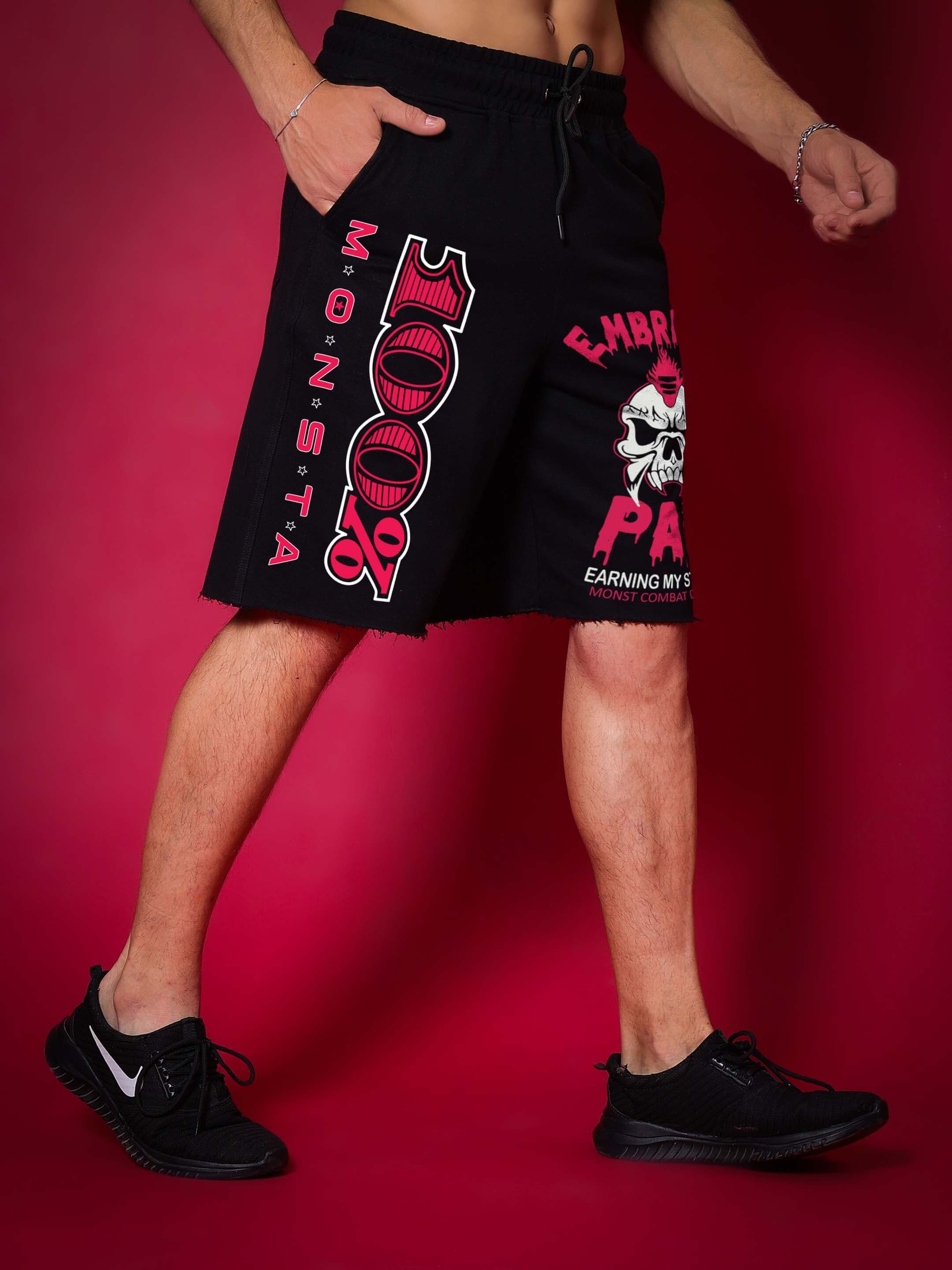 MONSTA Combat Regular Fit Black Shorts with bold graphics, shown on a model against a red backdrop, available in custom sizes.