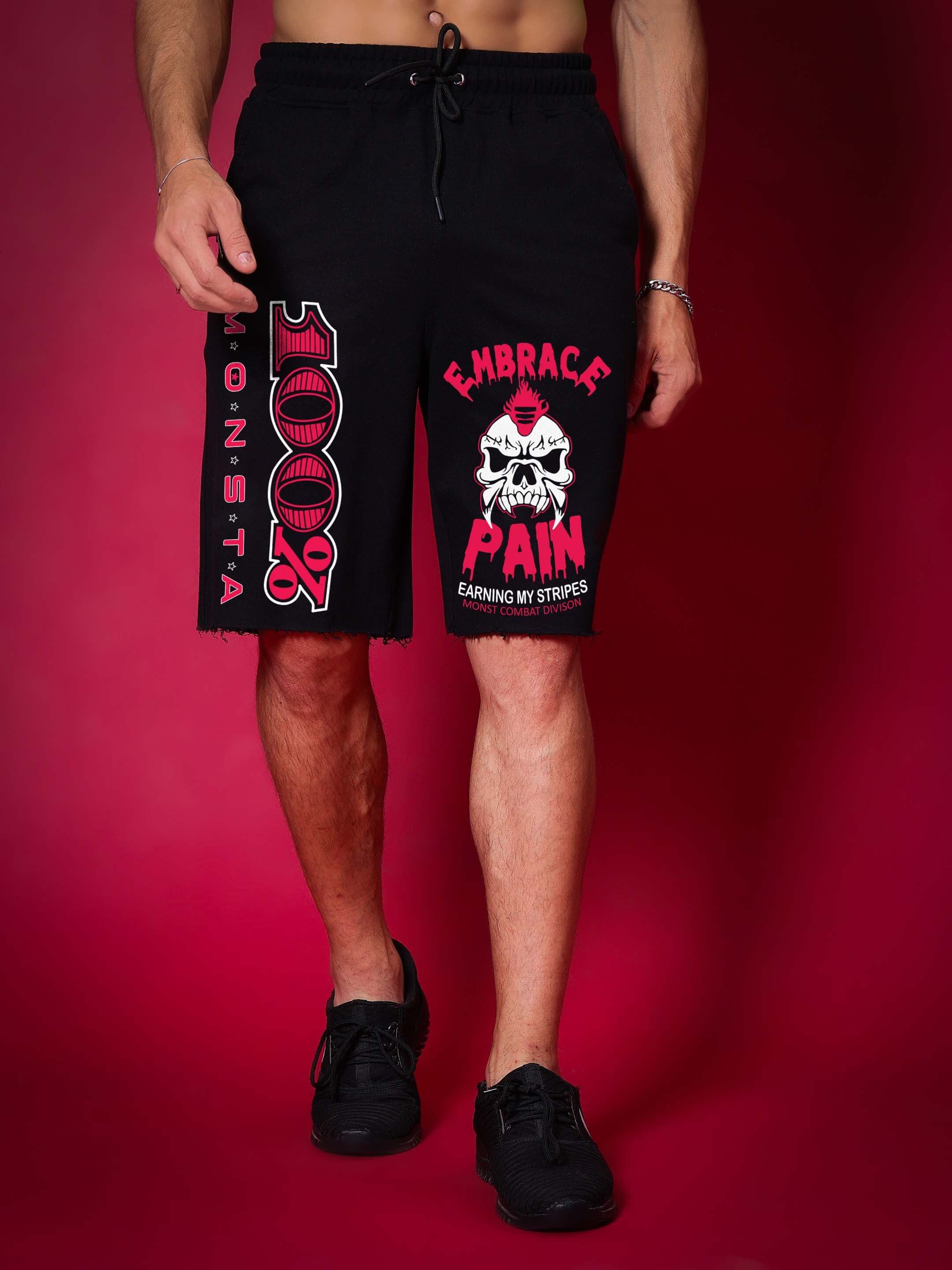 Person wearing MONSTA Combat Regular Fit Shorts in black with custom fit option available, featuring bold graphic designs.
