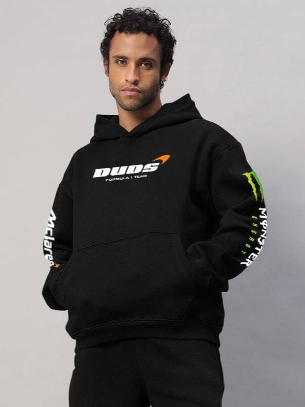 Model wearing MONSTER DRINK FLEECE HOODIE BLACK by DUDS with logo and text on sleeves.