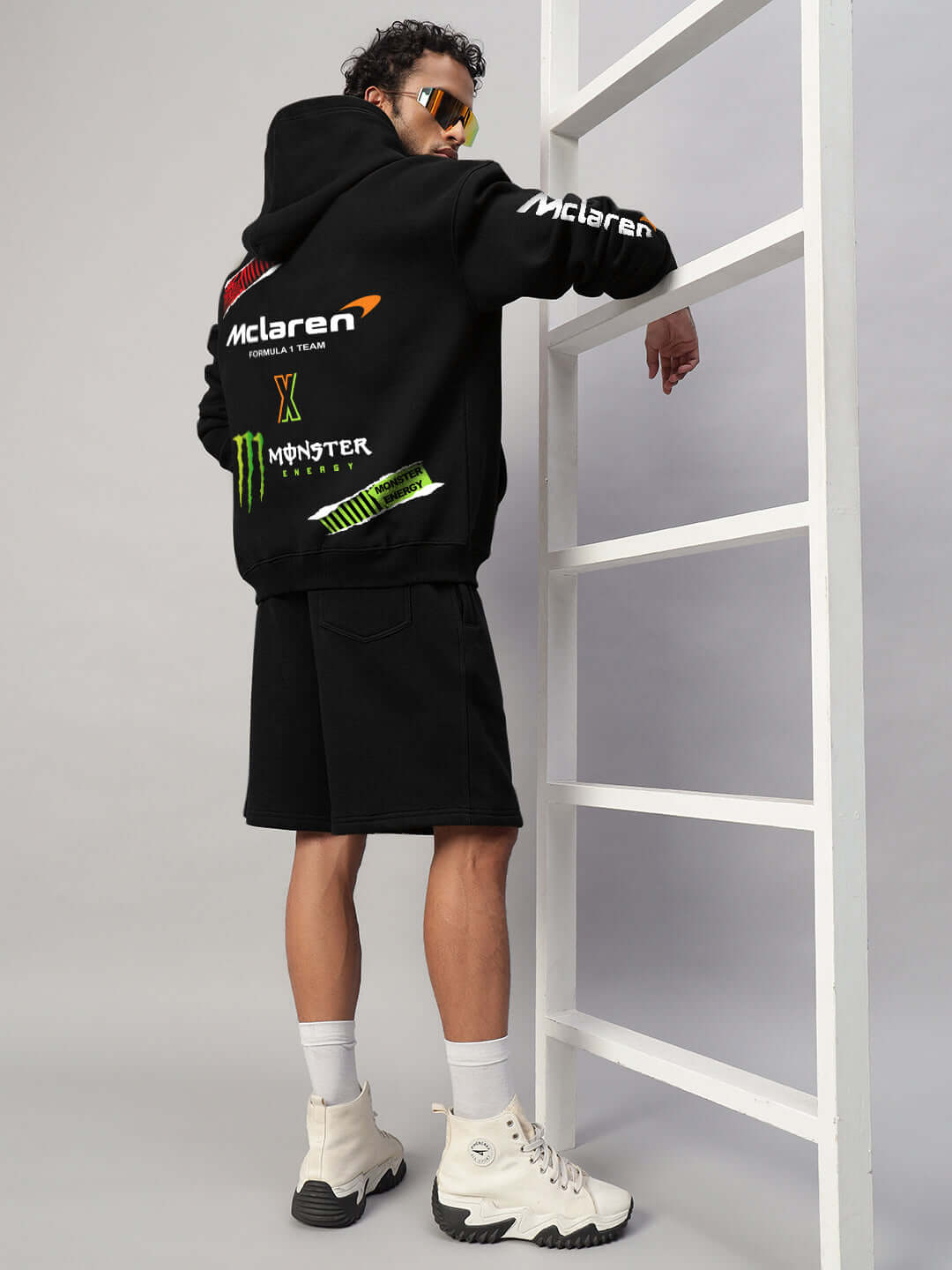 Back view of person wearing MONSTER DRINK FLEECE HOODIE BLACK with logos, standing on ladder.