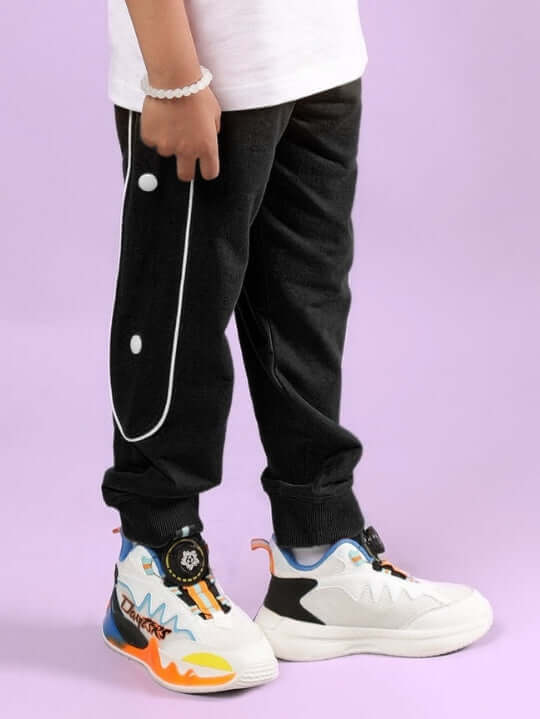 Child wearing MOON NIGHT JOGGER FOR BOYS & GIRLS BLACK with colorful sneakers on a pastel background.
