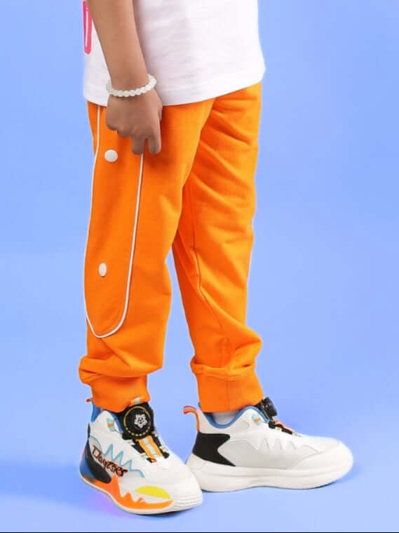 Child wearing bright orange jogger pants with stylish sneakers, standing against a blue background.