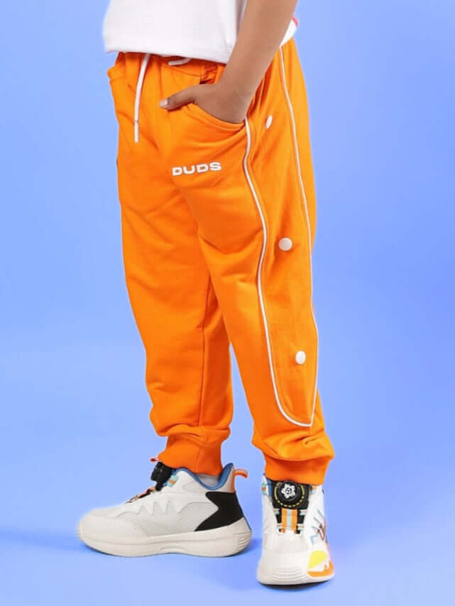 Child wearing orange MOON NIGHT JOGGER by DUDS, showcasing sporty design with white sneakers, perfect for boys and girls.