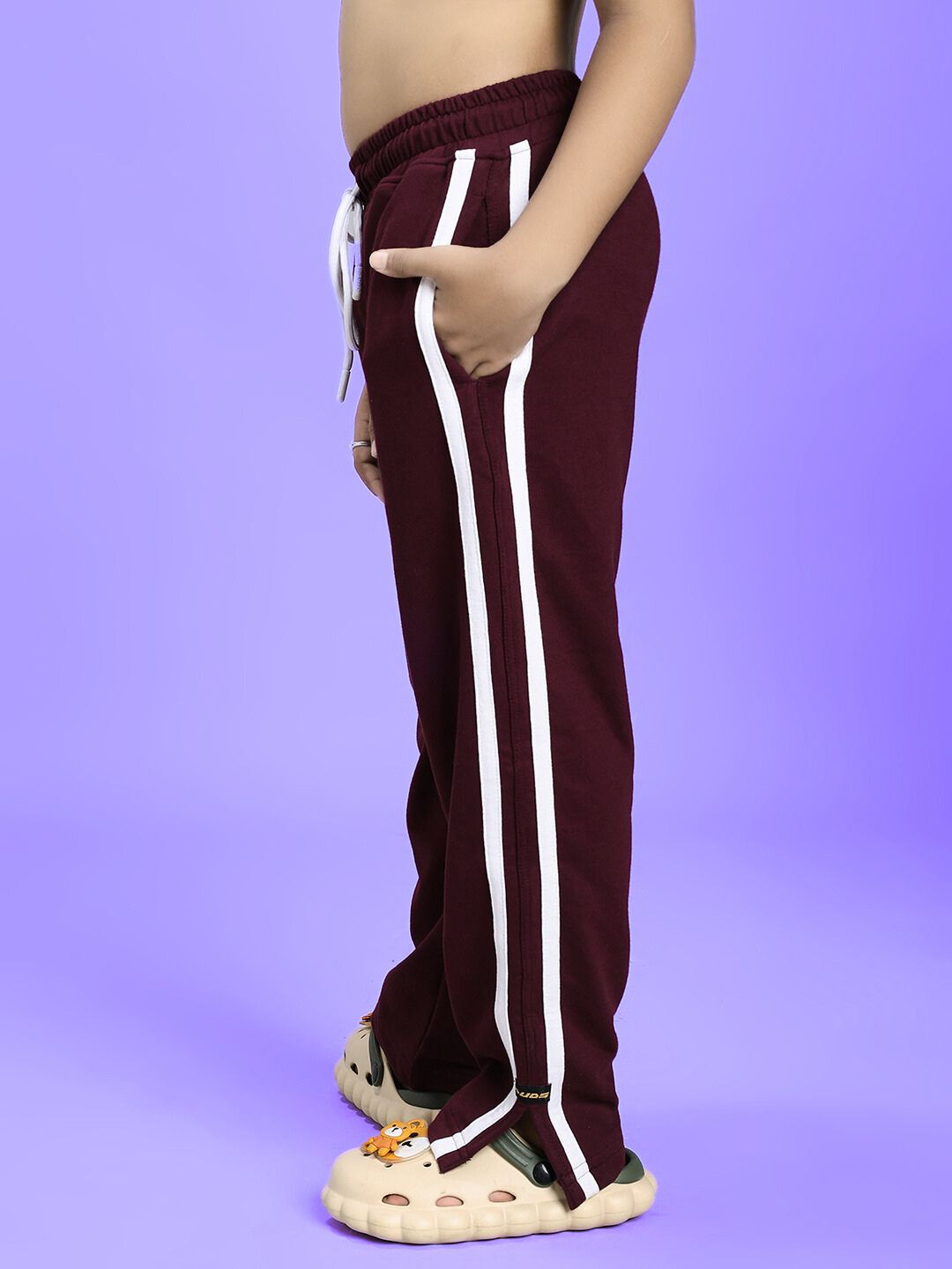Child wearing MOSCOW RELAXED FIT JOGGER FOR BOYS AND GIRLS MAROON with side stripes, shown from the side. Activewear fashion for kids.