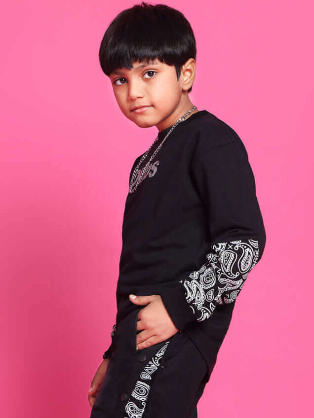 Child wearing black motif joggers, showcasing intricate pattern sleeves against a vibrant pink background, expressing trendy fashion.