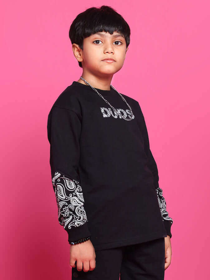 Child wearing MOTIF JOGGERS for boys and girls in black, designed by DUDS, featuring unique sleeve patterns, on a pink background.