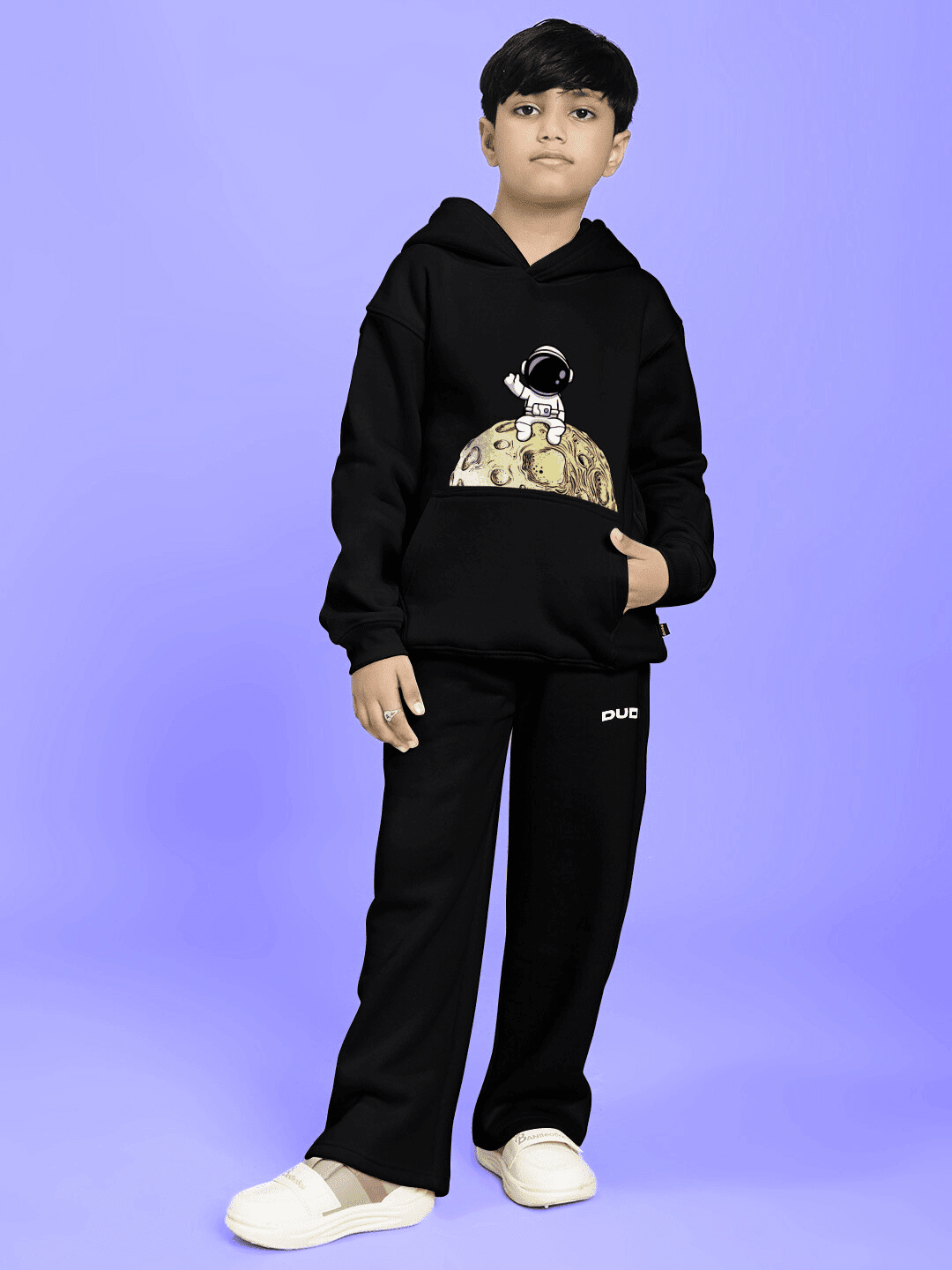 Boy wearing NEXT TO A MOON FLEECE CO-ORD FOR BOYS AND GIRLS BLACK, featuring an astronaut graphic, on a blue background.