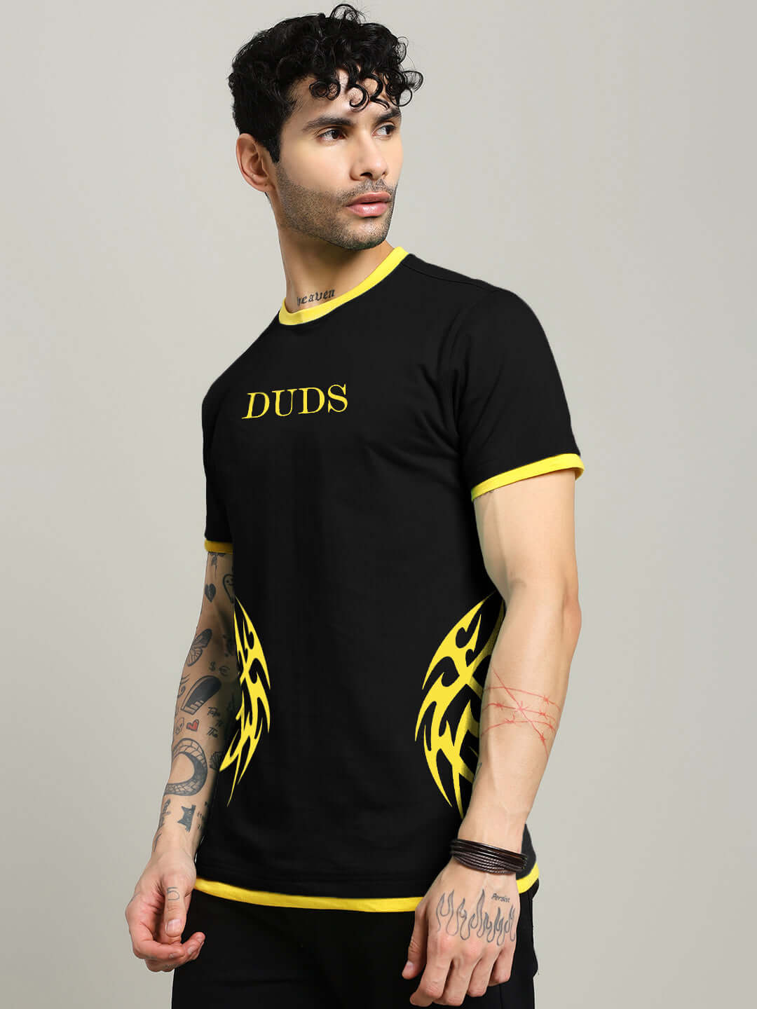 Model wearing black NIMO regular fit T-shirt with yellow trim and tribal print, crafted from 100% cotton, displaying 'DUDS' text on chest.